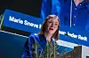 Marie Sneve Martinussen står ved en talerstol med blomster foran en blå bakgrunn med Rødt-skilt.