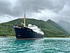 Passasjerskipet MS «Salten» ligger på turkis fjordvann foran grønne, bratte fjell under en skyet himmel.