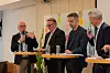 Fire menn deltar i en panelsamtale ved et bord med mikrofoner og vannglass i et møterom.