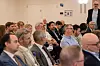 Møte­deltakere sitter på rekke i et konferanserom, mens en mann står bakerst til høyre.