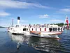 Det hvite hjuldampskipet Skibladner seiler på Mjøsa med passasjerer om bord og norske flagg i akterenden.