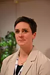 Portrett av en kortklipt kvinne i lys blazer med adgangskort, fotografert innendørs.