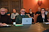 En gruppe mennesker sitter samlet rundt et bord i et møterom, med en bærbar PC sentralt i bildet.